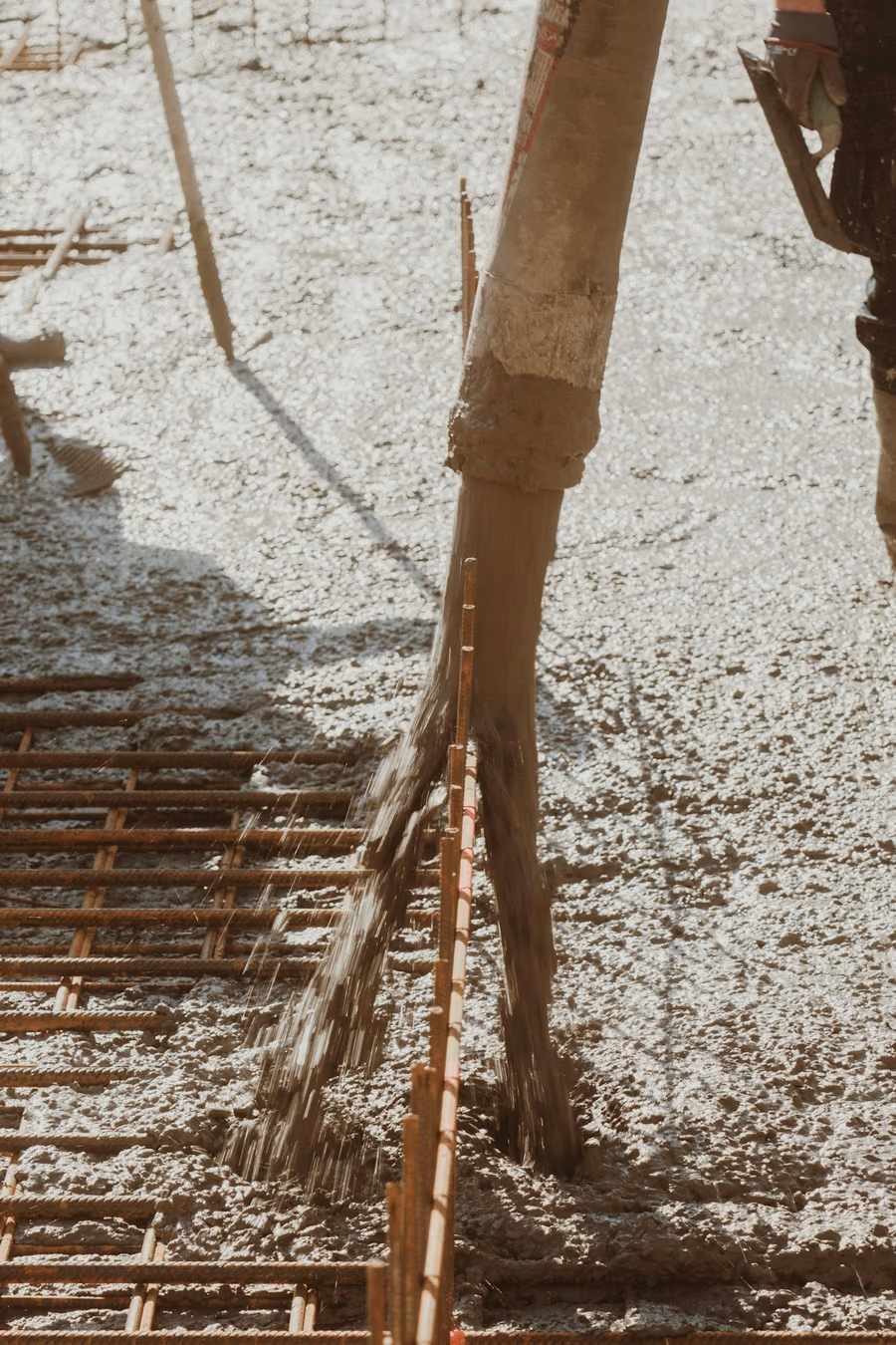 A concrete pump boom discharging fresh concrete over a tied steel reinforcement grid in bright sunlight