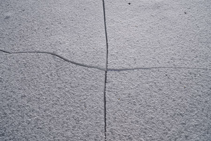 Close view of a concrete slab where a straight sawcut control joint meets a narrower crack that has wandered across the surface